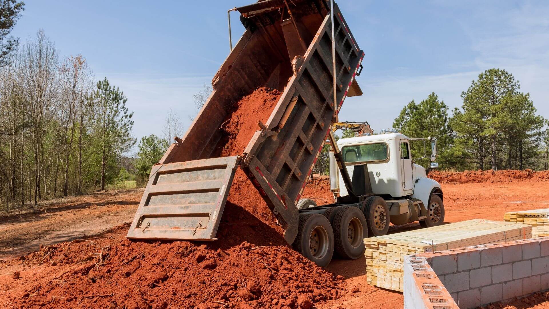 Dump truck unloading soil at construction site covered by trucking insurance in Stockton